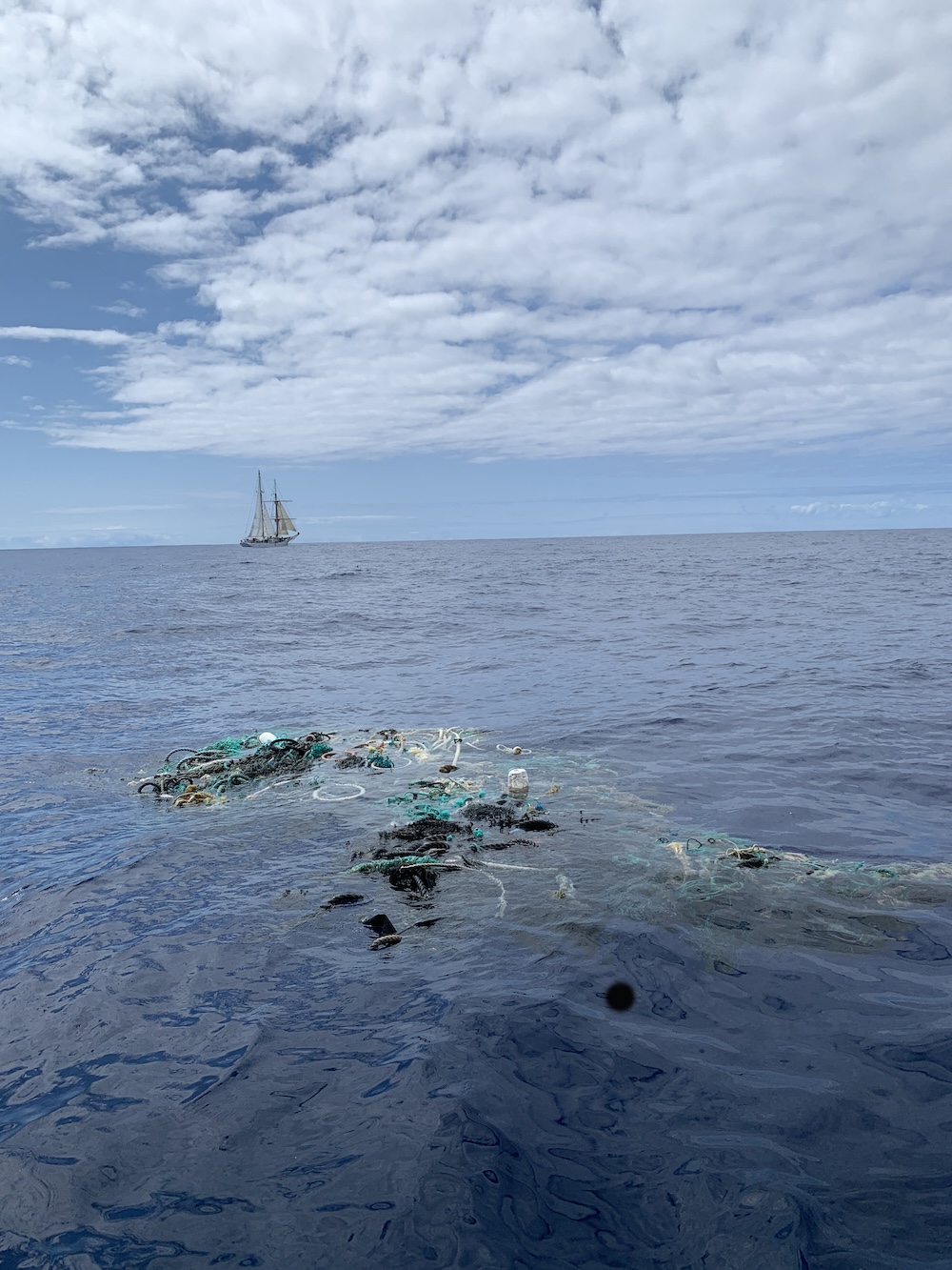 Plastic floating in the ocean with a sailing ship in the background